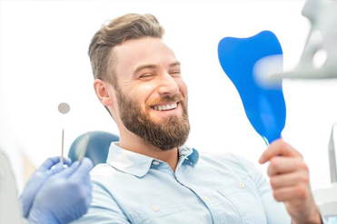 Man smiling looking in dental mirror